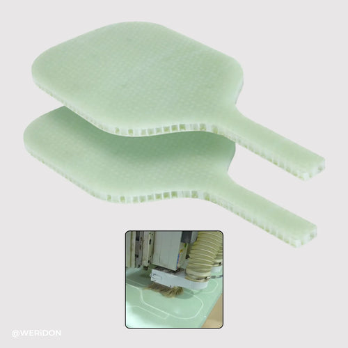 Two green cold pressed paddles stacked on a white background with a small inset showing a machine in the process of cutting them.